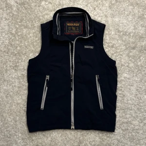 Mörkblå Woolrich väst - Säljer en snygg mörkblå väst från Woolrich med dragkedja och broderad logga på bröstet. Lite tunnare så passar bra till varmare vårdagar.  Storleken är s men den passar mer som xs.              Skick 8/10                     Hör gärna av dig vid frågor!                     