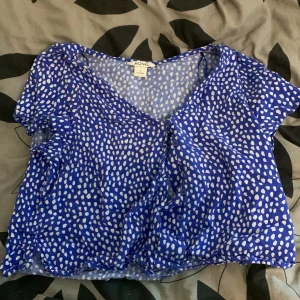 Blå prickig blus från Monki - Säljer en blå blus från Monki med vita prickar. Blusen har korta ärmar och en luftig passform, perfekt för varmare dagar. Tillverkad i 100% viskos vilket ger ett mjukt och skönt fall. Ett härligt tillskott till garderoben för en färgglad look!