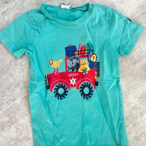Turkos t-shirt med sherifftryck - Säljer en turkos t-shirt från Polarn O. Pyret med ett färgglatt tryck av en sheriffbil och djur. Perfekt för barn som gillar äventyr och lek. T-shirten har korta ärmar och är gjord i mjukt material.