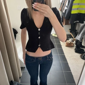 Svart kortärmad topp  - Supersnygg tröja med knappar från Gina. Silvriga knappar och det följer även med en extra knapp! Knappt använd, säljer för att jag inte har använt den sen jag köpte den😊
