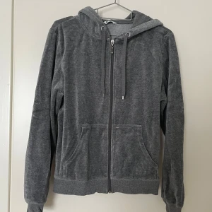 Grå hoodie i velour - Mysig grå hoodie i mjukt velourmaterial med dragkedja framtill och justerbar huva. Perfekt för en avslappnad stil. Den har långa ärmar och ribbade muddar vid ärmslut och nederkant.