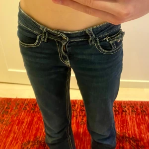 Mörkblå jeans med Union Jack-detalj - Snygga mörkblå jeans med låg midja och en cool Union Jack-detalj på bakfickan. Jeansen har en tight passform och klassisk femficksdesign med dragkedja och knapp framtill. (Pris kan diskuteras) (har endast använt dem någon enstaka gång) 