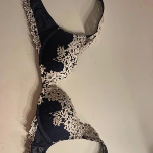 Intimissmi BH - Elegant marinblå bh med vackra spetsdetaljer och broderier i vit. Den har justerbara axelband och en klassisk hakknäppning bak. Perfekt för att ge en lyxig känsla till vardagsoutfiten. St 80B