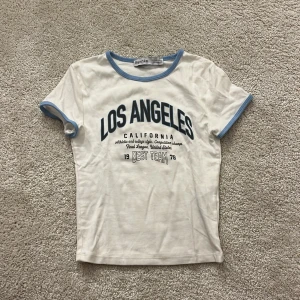 Vit t-shirt från Bershka med Los Angeles-tryck - Vit t-shirt från Bershka med blå detaljer och tryck med texten 'Los Angeles California'. Kortärmad och i mjukt bomullsmaterial. 
