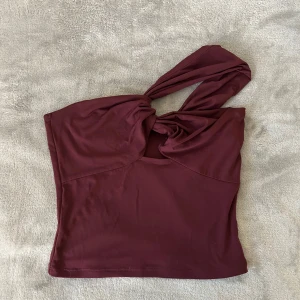 Vinröd oneshoulder topp från BikBok - Säljer den här snygga vinröda oneshoulder toppen från BikBok. Säljer då den är för liten💕
