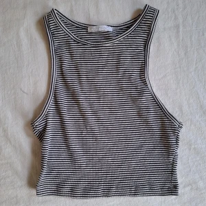 Randig ribbad samt kroppad linnetopp - Säljer en randig ribbad linnetopp i svart och vit. Toppen är ärmlös och har en enkel design som passar perfekt för varma dagar. Den är tillverkad i ett mjukt och bekvämt material.