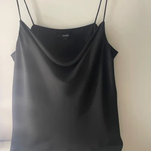 Svart linne från Lindex - Snyggt svart linne från Lindex med tunna axelband och en elegant drapering framtill. Perfekt för en stilren look.