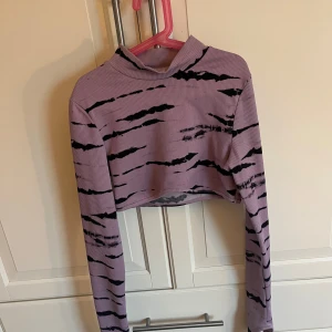 Lila croppad tröja - Säljer en cool lila croppad tröja med svart zebramönster. Tröjan har långa ärmar och är ribbad med hål för tummarna.