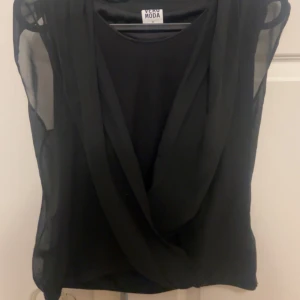 Svart ärmlös topp från Vero Moda - Snygg svart ärmlös topp från Vero Moda med ett draperat framstycke. Perfekt för en stilren look. Tillverkad i ett lätt och luftigt material.