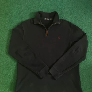 Svart tröja med dragkedja från Polo Ralph Lauren - Snygg marinblå tröja från Polo Ralph Lauren med halv dragkedja och ikonisk röd logga på bröstet. Perfekt för en stilren look. Tröjan har långa ärmar och en bekväm passform.                                                      Pris kan diskuteras!