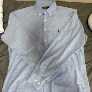 Polo Ralph Lauren skjorta - Snygg blå skjorta från Polo Ralph Lauren med klassisk krage och broderad logga på bröstet. Skjortan har långa ärmar och knappar framtill. Perfekt för en stilren look. 