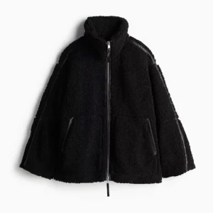 Svart teddyjacka med dragkedja - Mysig svart teddyjacka med dragkedja framtill och hög krage. Jackan har en oversized passform och två fickor på sidorna. Perfekt för kyliga dagar när du vill hålla dig varm och stilren.