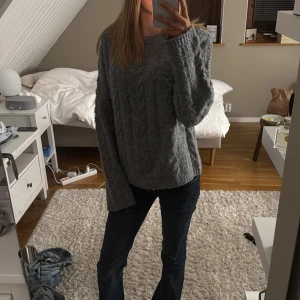 Grå stickad tröja - Mysig grå stickad tröja med kabelstickat mönster. Perfekt för kyliga dagar med sin avslappnade passform och långa ärmar.