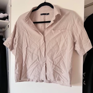 Beige kortärmad skjorta - Säljer en stilren beige kortärmad skjorta från Lager157. Skjortan har en klassisk krage och knappar framtill. Perfekt för en avslappnad look. Använd 1-2 gånger. Önskar du veta exakta mått? Tveka inte att höra av dig!