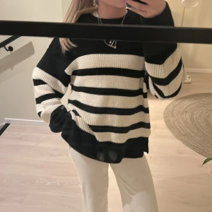 Randig stickad tröja från Gina Tricot - Säljer en snygg svart och vit randig stickad tröja från Gina Tricot. Tröjan har långa ärmar och en bekväm passform, perfekt för en stilren look. Den är gjord i ett mjukt material som håller dig varm och bekväm. Perfekt för kyligare dagar!