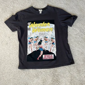 Mörkgrå Wonder Woman t-shirt från H&M - Säljer en cool svart t-shirt från H&M med ett Wonder Woman-tryck på framsidan. T-shirten är kortärmad och gjord i mjuk bomull för en bekväm passform. 