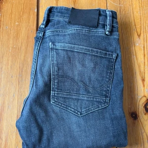 Mörkblå jeans från Jack & Jones - Snygga mörkgrå jeans från Jack & Jones med klassisk femficksdesign och knappgylf. Jeansen har en slim-straight passform och är perfekta för en avslappnad stil. De är tillverkade i slitstarkt denim och har en subtil tvätt för en modern look.