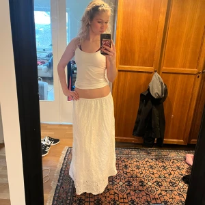 Vit långkjol från H&M - Säljer en vacker vit långkjol från H&M med broderade blommor. Kjolen har en elastisk midja med knytband för extra komfort. Perfekt för en kylig vår morgon eller sommar kvällar💕priset kan diskuteras🥰