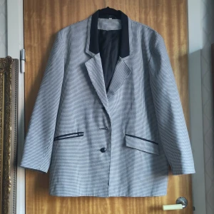 Rutig kavaj med svarta detaljer - OBS! Saknar mittenknappen. Snygg rutig kavaj med svarta detaljer och knappar. Den har en klassisk krage och två fickor framtill. Perfekt för en stilren look.