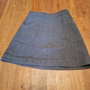 Grå kjol från Monki - Snygg grå kjol från Monki i en klassisk design. Kjolen har två fickor framtill och en bekväm passform. Perfekt för en stilren look.