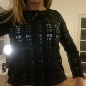 Svart nätmönstrad tröja - Snygg svart tröja med nätmönster som ger en cool look. Perfekt för att lägga över ett linne eller topp. Tröjan har långa ärmar och en rund halsringning.