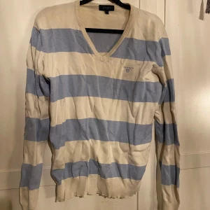 Randig tröja från Gant - Säljer en randig tröja från Gant i beige och blått. Tröjan har en v-ringad hals och långa ärmar. Perfekt för en avslappnad stil. Hör av dig vid intresse!