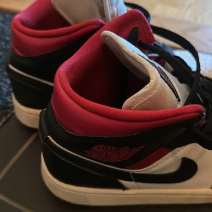 Nike Air Jordan 1 svart/röd/vit - Säljer ett par Nike Air Jordan 1 med klassisk färgkombination i svart, rött och vitt. Skorna har högt skaft, svart swoosh, perforerad tå och snörning. Ovandelen är i skinn och de ikoniska Air Jordan-detaljerna syns på sidan. Perfekta för dig som gillar streetstyle.