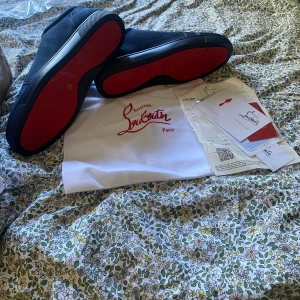 Christian Louboutin mörkblå sneakers - Exklusiva svarta sneakers från Christian Louboutin i mocka med ikonisk röd sula och broderad logga på hälen. Snygg och stilren design med rund tå och platt sula. Kommer med dustbag och äkthetskort.