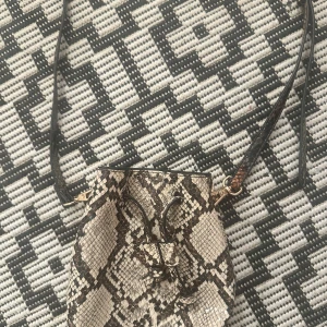 Axelväska i ormmönstrat skinn - Säljer en snygg axelväska med ormmönster i beige och svart. Väskan har justerbar axelrem, dragskostängning och detaljer i guld. Perfekt för dig som vill sticka ut med en trendig accessoar.