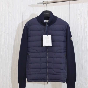 Mörkblå Moncler cardigan! - Snygg mörkblå pufferjacka från Moncler med quiltad framsida och stickade ärmar. Jackan har dragkedja hela vägen, hög krage och diskret Moncler-logga på ärmen. Perfekt för dig som vill ha en stilren och sportig look.