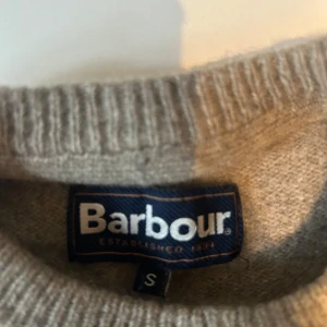 Grå stickad tröja Barbour med mockadetaljer - Grå stickad tröja från Barbour i storlek S. Klassisk modell med rund hals och ribbade muddar. Tröjan har  mockadetaljer på armbågarna. Ett pyttelitet hål vid axeln men syns knappt. Hör av er vid frågor.//Nypris 1250kr.