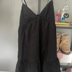 Svart kort klänning från BikBok - Supersöt svart kort klänning från BikBok med smala axelband och v-ringning. Klänningen har volang nertill och snörning i ryggen för en snygg passform. Perfekt för dig som gillar en enkel men trendig stil.