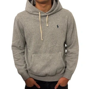 Grå hoodie från Polo Ralph Lauren - Snygg grå hoodie från Polo Ralph Lauren med klassisk broderad logga på bröstet. Tröjan har huva med snörning, känguruficka och ribbade muddar. Perfekt för en chill och stilren look. Tillverkad i mjuk bomullsmix för extra komfort. Modellen är 182cm.