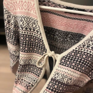 Mönstrad kofta från Capri Collection - Superfin kofta från Capri Collection med snyggt mönster i rosa, svart och beige. Koftan har lång ärm, v-ringning och knytning framtill. Perfekt för dig som gillar stickade plagg med unika detaljer och mysig känsla.