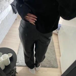 Svarta raka byxor i skinnimitation - Snygga svarta byxor i skinnimitation med raka ben och låg midja . De har klassiska fickor fram och en stilren look som passar till många outfits. Perfekta för dig som gillar en trendig och clean stil.
