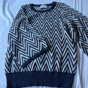 Mönstrad tröja från Neo Noir - Säljer en stickad tröja från Neo Noir med svartvitt zigzag-mönster. Materialet är mjukt och har en lätt glittrig effekt. Armarna är trekvartsärm!