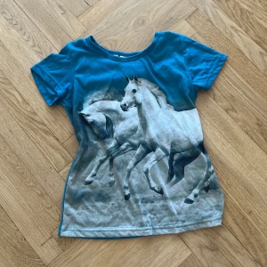 Unik topp - Unik graphic tee med två vita hästar. Jättefin petrolblå färg. 