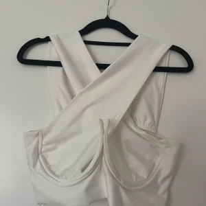 Vit korsettinspirerad croppad topp - Säljer en vit croppad topp med breda axelband som korsas i ryggen.