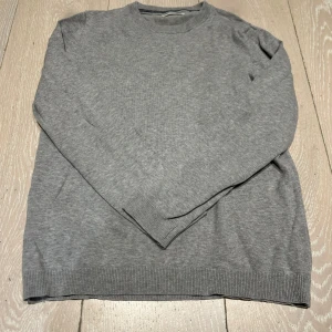 Grå stickad tröja från MNG - En basic grå stickad tröja från MNG med rund halsringning och ribbade muddar vid ärmslut och nederkant. Perfekt för lager-på-lager och enkel att matcha med allt. Mjuk och skön känsla, passar dig som gillar en clean och stilren look. Den passar 152 cm men lite på gränsen om man är längre. Tvekca inte för att höra av er😊