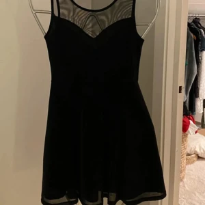 Svart kort klänning från H&M Divided! Oanvänd!  - Snygg svart klänning från H&M Divided med transparent mesh upptill och smala axelband. Perfekt för en stilren look. Klänningen har en kort längd och en lätt utsvängd kjol som ger en fin silhuett.  Kjolen är fodrad. Klänningen är aldrig använd. 
