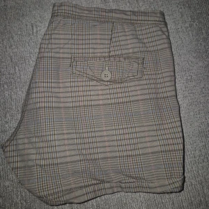 Rutiga shorts - Rutiga shorts i beige och bruna toner med inslag av blått och rosa. Tillverkade i 100% bomull, har bakfickor med knapp. Klassisk passform med låg midja.