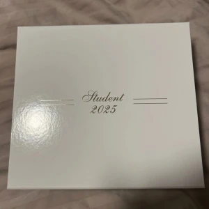 Vit studentbox 2025 från Crownstudent - Snygg och stilren vit box med texten 'Student 2025' i guld på locket. Perfekt för att spara minnen från studenten. Insidan har texten 'Ett minne för livet...' och en liten krona. Helt oanvänd. 