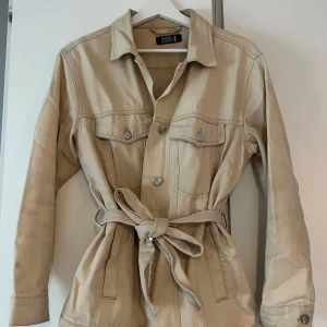 Beige jeansjacka  - Snygg beige jeansjacka från Even&Odd med klassisk krage, knappar framtill och två bröstfickor. Jackan har ett avtagbart bälte i midjan för en mer markerad siluett. Perfekt för lager-på-lager och enkel att styla till olika outfits.