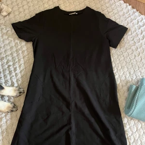 Svart t-shirtklänning från me&i XL - Enkel svart t-shirtklänning från me&i i storlek XL. Klänningen har rund halsringning, korta ärmar och är tillverkad i mjuk bomull. Den har en rak passform och är perfekt för en chill och stilren look.