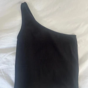 Svart oneshoulder topp Gina Tricot - Säljer en svart ribbad oneshoulder topp från Gina Tricot i storlek XS. Toppen har en tight passform och är tillverkad i ett stretchigt material som sitter snyggt på kroppen. Perfekt för dig som gillar stilrena och trendiga plagg.