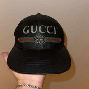Svart keps från Gucci i skinn - Snygg svart keps från Gucci med klassisk logga framtill och gröna/röda ränder. Framsidan är i skinn och baksidan har mesh-tyg för extra ventilation. Justerbar passform.                     Väldigt bra skick!                                               Storlek M 