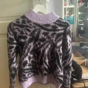 Lila zebramönstrad stickad tröja - Supermjuk stickad tröja i lila med svart zebramönster. Tröjan har en hög ribbad krage och långa ärmar. Passformen är normal och materialet känns fluffigt och varmt. Aldrig använd varav superbra skick!💜💜 Har inga bilder med den på