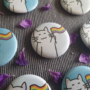 Egentillverkade katt pride-pins! - 🐱Pins/knappar med en vit katt och en prideflagga på 🏳️‍🌈 Finns med blå bakgrund och vit bakgrund. Detta är första sorteringen, alltså är dessa i mycket bra skick. Det finns andra sorteringens också, och de är billigare men också sämre kvalitet. 🗣️ Det finns många utan text men även några få som det står “Heja!“ på. ✨Jag har både designat och tillverkat dem själv!