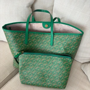 Grön shoppingväska från Guess - Snygg shoppingväska från Guess i grönt och beige med grafiskt mönster och matchande mindre väska som går att fästa inuti den större väskan. Väskan har två handtag, magnetknapp och ljusrosa foder med Guess-logga. Perfekt för dig som vill ha plats för allt och ändå se trendig ut.