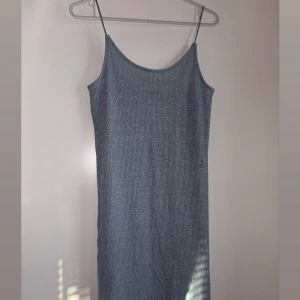 Glittrig långklänning med tunna axelband - Snygg långklänning i glittrigt mörkgrått tyg med tunna axelband och rak passform. Klänningen har en enkel, stilren look och är perfekt för dig som vill sticka ut med lite extra shimmer. Materialet känns mjukt och följsamt mot kroppen.